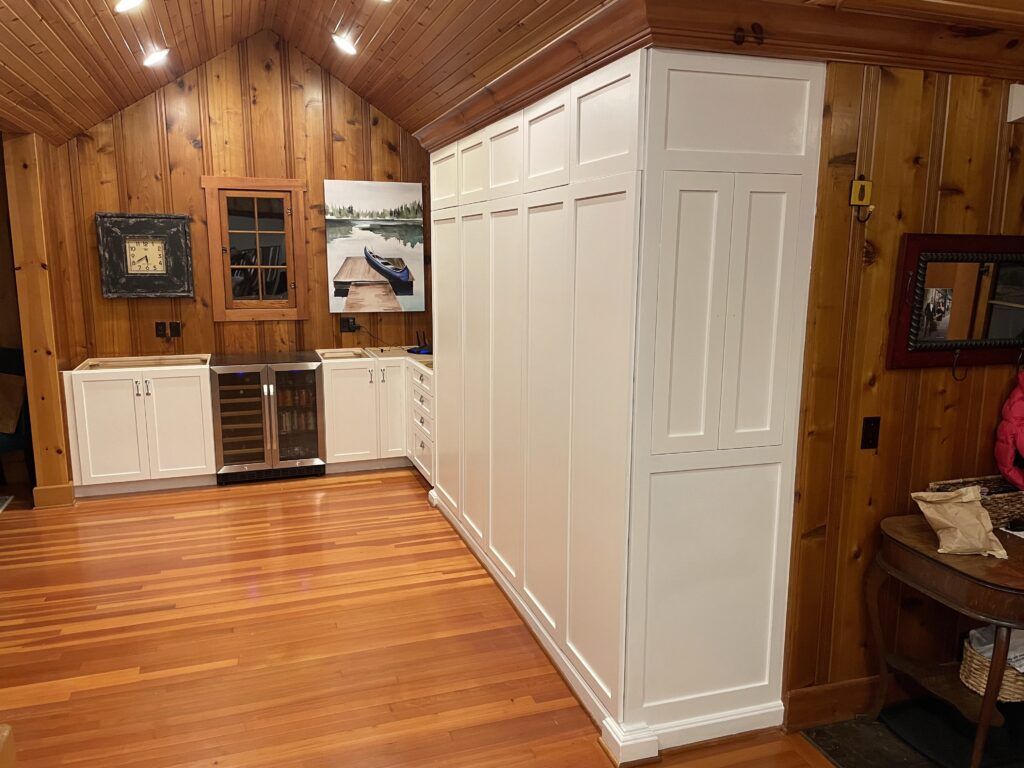 White built-in cabinets in a room with wood paneling and hardwood floors. A wine cooler and framed art are visible.