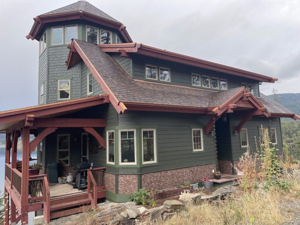 Green house with a tower and a brown roof. Deck with a view.