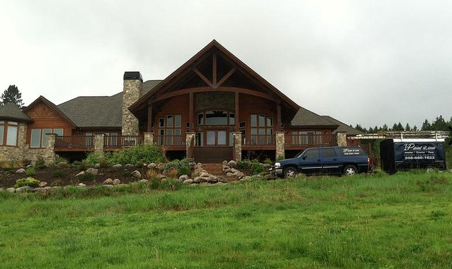 Large wooden house with stone chimney, surrounded by green grass and a cloudy sky.
