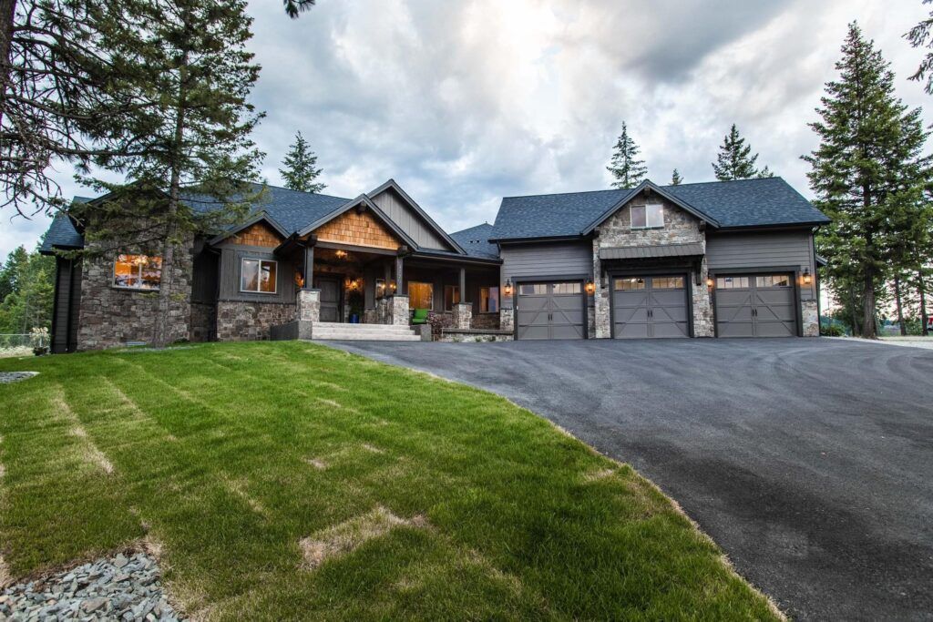 A modern, gray-colored house with a three-car garage and a stone facade, set against a cloudy sky.