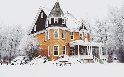 Yellow brick house with a turret and porch, covered in snow; winter setting.