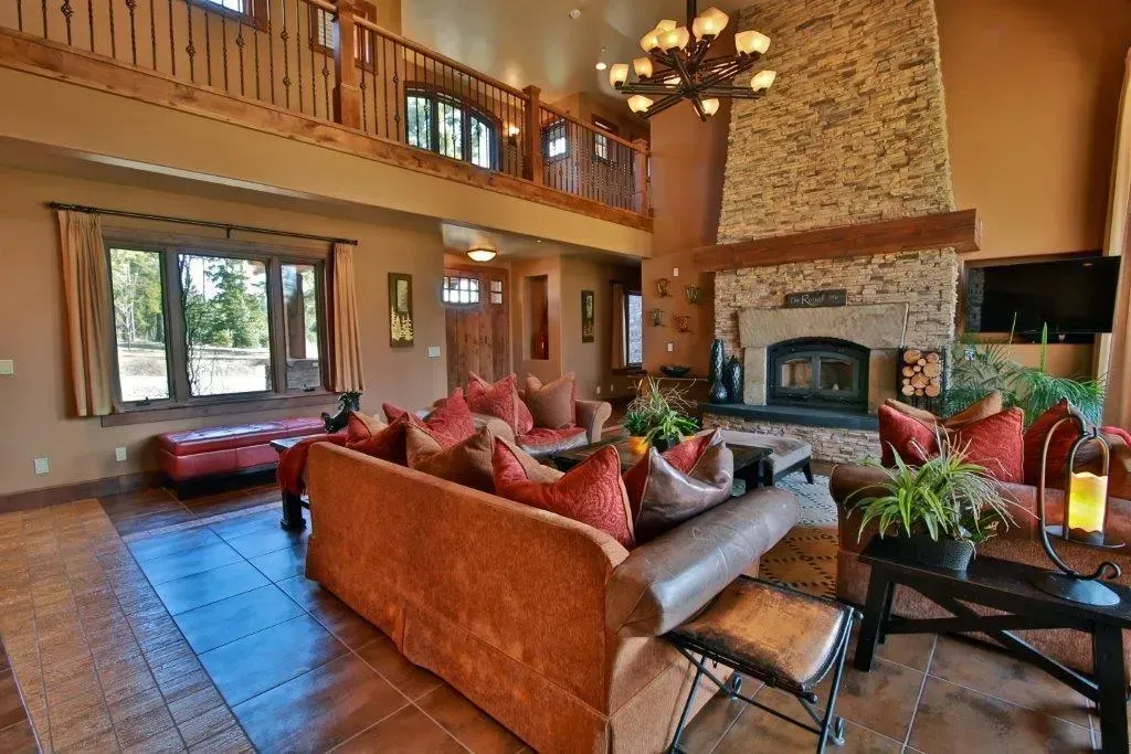 Spacious living room with a stone fireplace, large windows, and a loft area with a brown couch and orange throw pillows.
