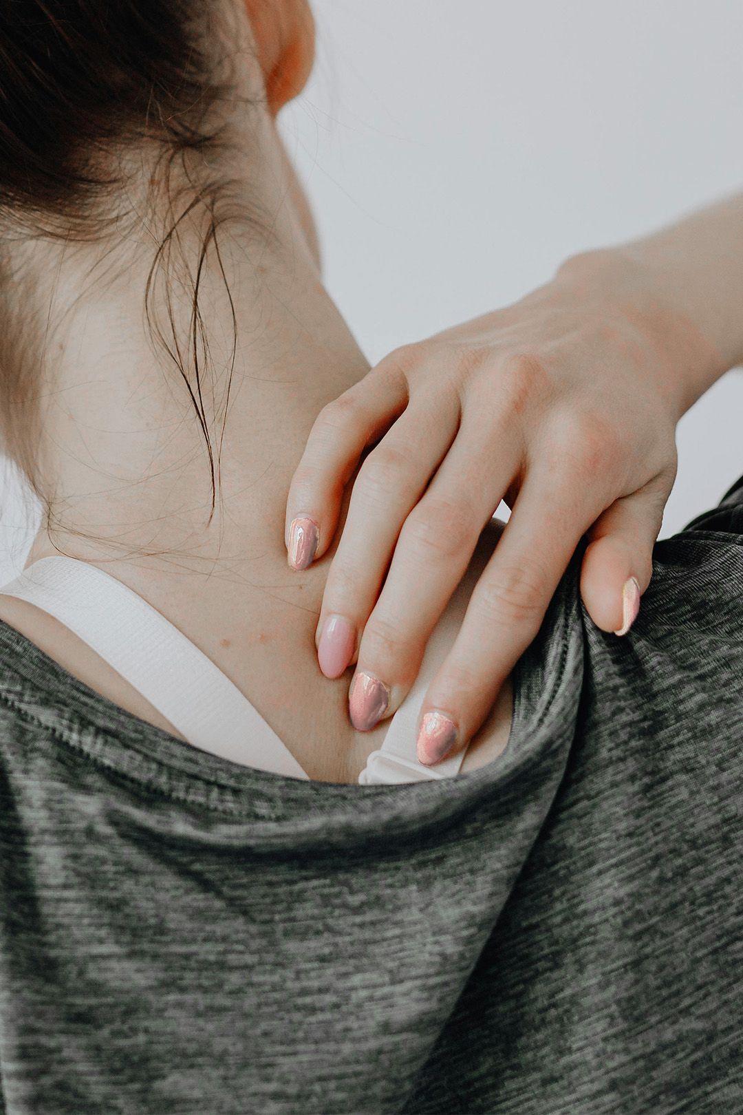 Person with hand on shoulder, possibly in pain. Small neck tattoo.