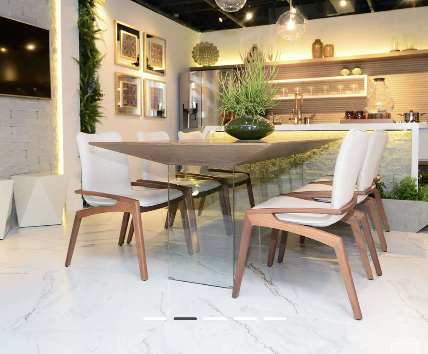 Comedor con mesa de madera, base de cristal, sillas blancas y plantas decorativas con losa Marmo D’Oro.