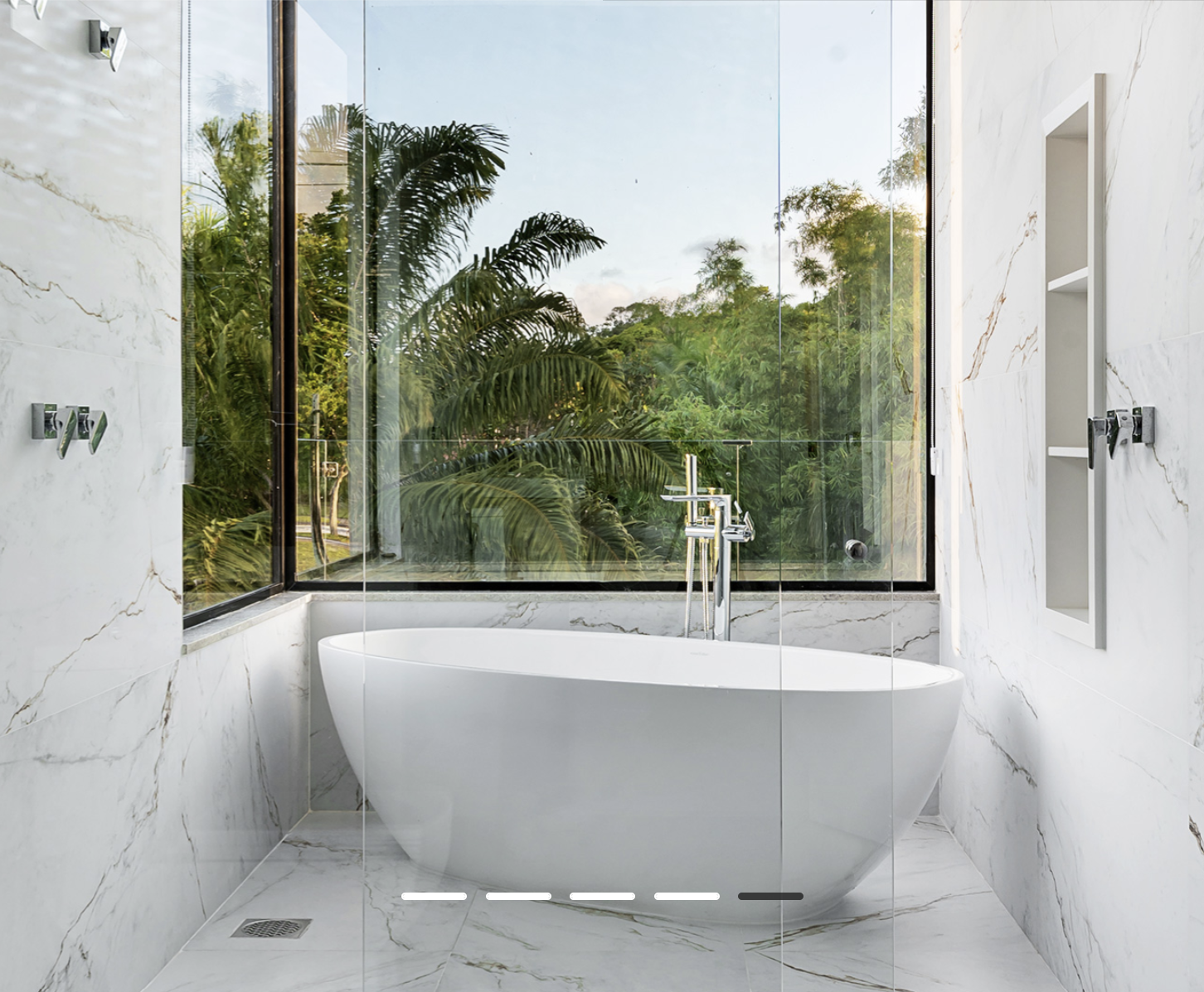 Un baño de lujo con bañera blanca y ventana panorámica hacia un paisaje natural, enmarcado por la elegancia atemporal de la losa Marmo D’Oro.