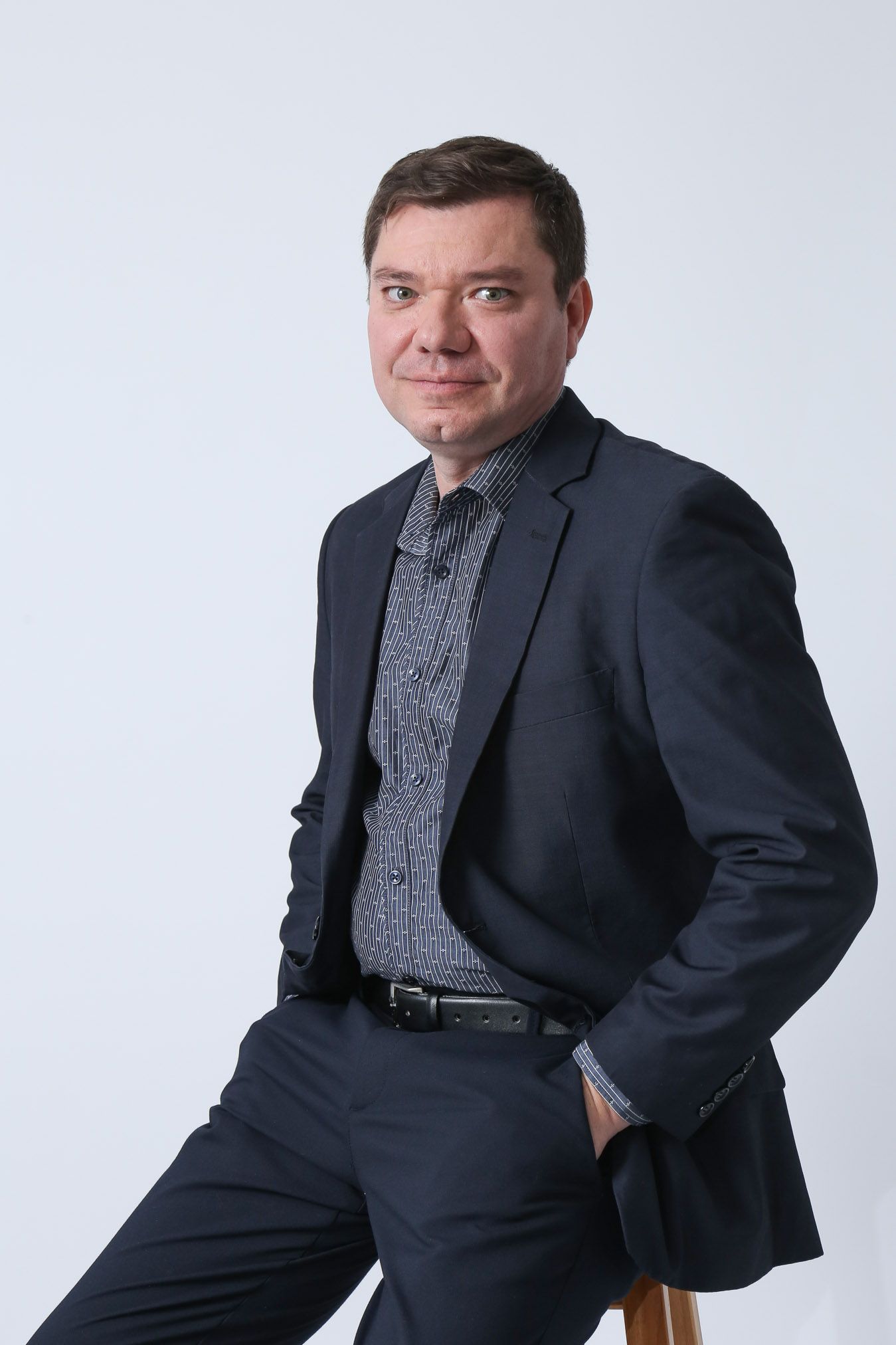 Homem de terno, sentado com a mão no bolso, olhando para a câmera contra um fundo branco.