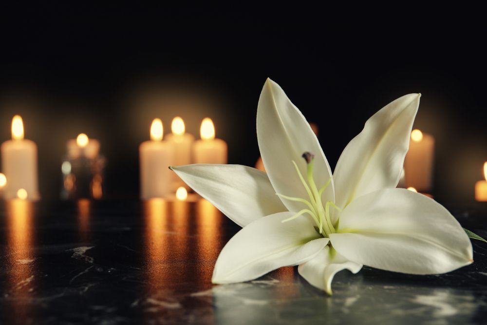 A White Lily Is Sitting on A Table in Front of Lit Candles  - A Better Way Funerals in St Leonards, NSW