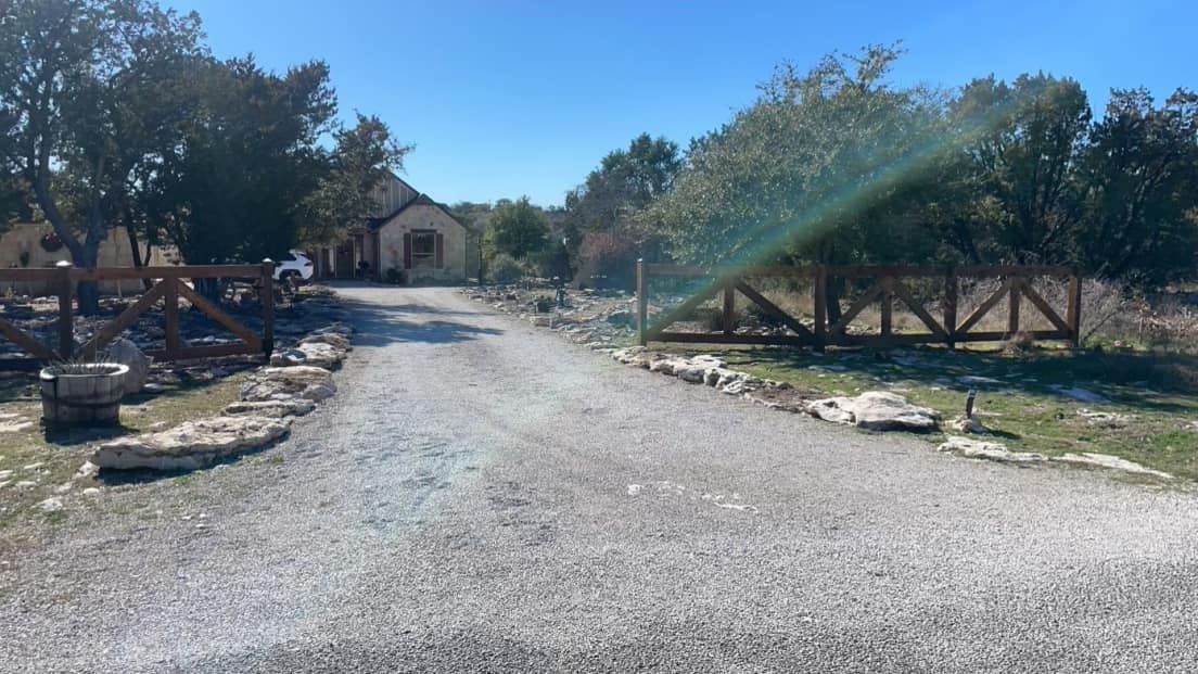 Gravel driveway leading to a house with a wooden fence on a sunny day.