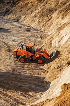 Orange wheel loader in a sand pit, scooping material.