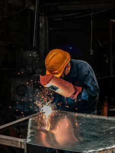Welder in a workshop, wearing a helmet and gloves, welding metal, sparks flying.