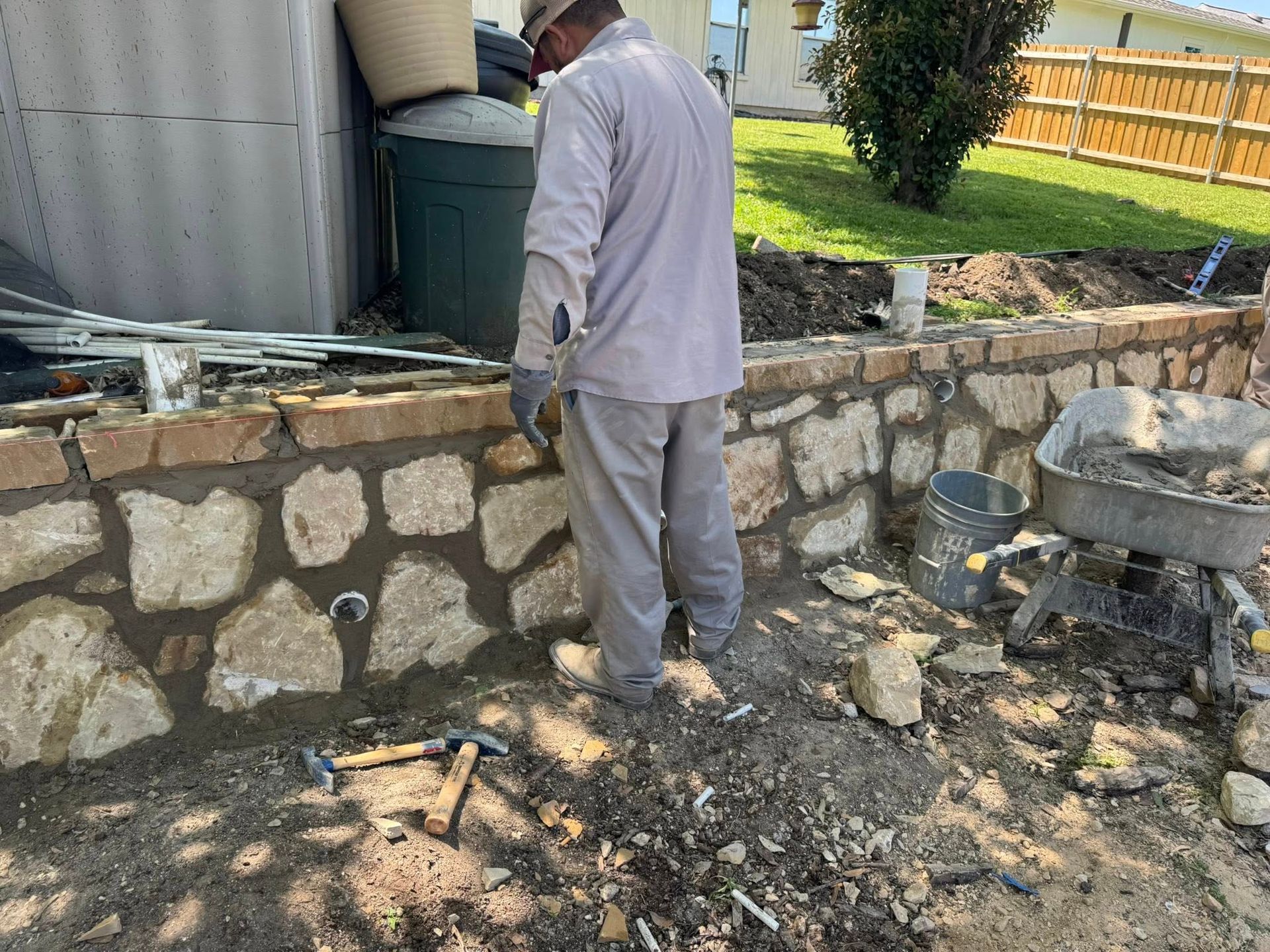 Man in work clothes building a stone retaining wall outdoors.