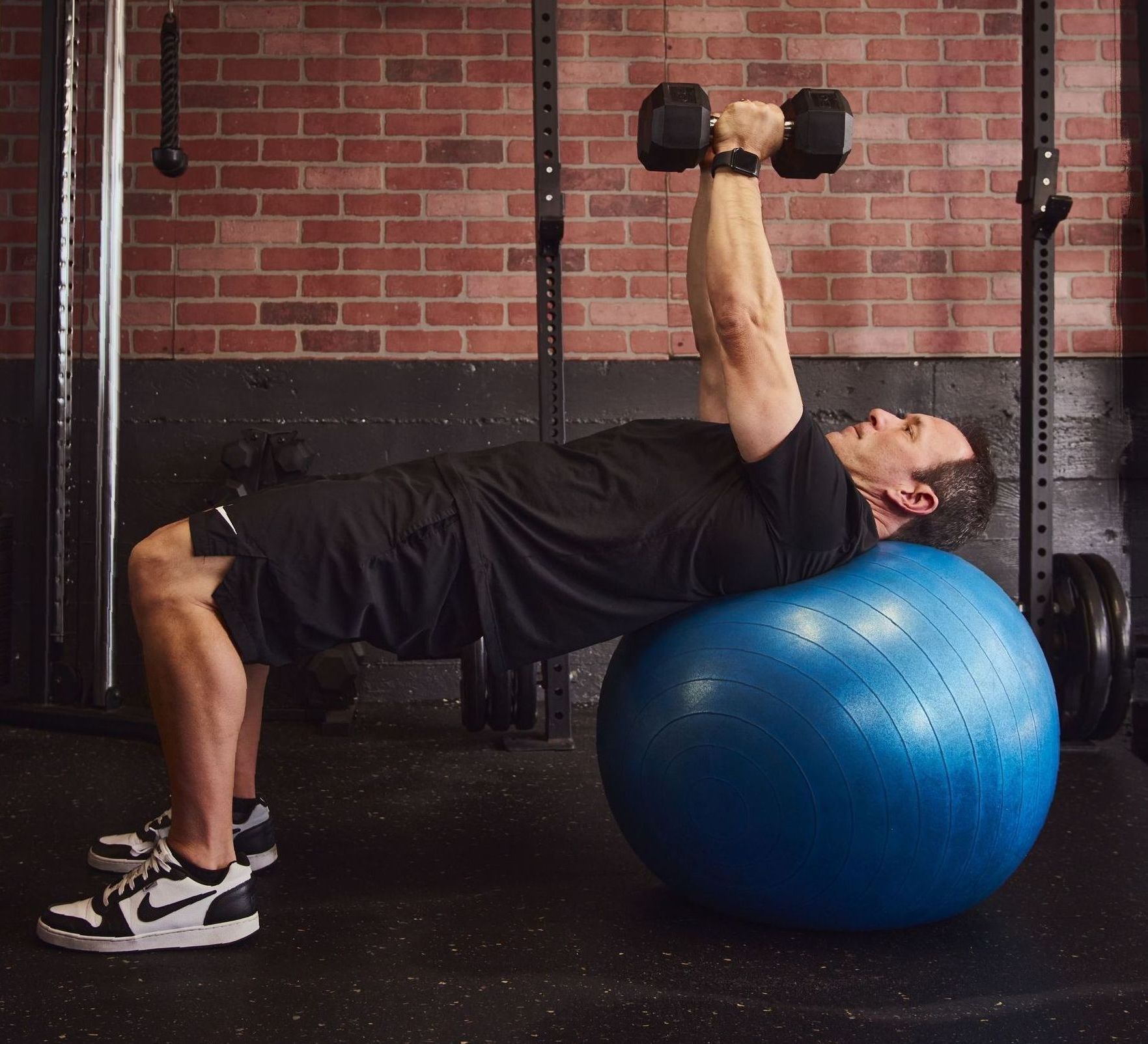 A man is laying on a blue exercise ball lifting dumbbells