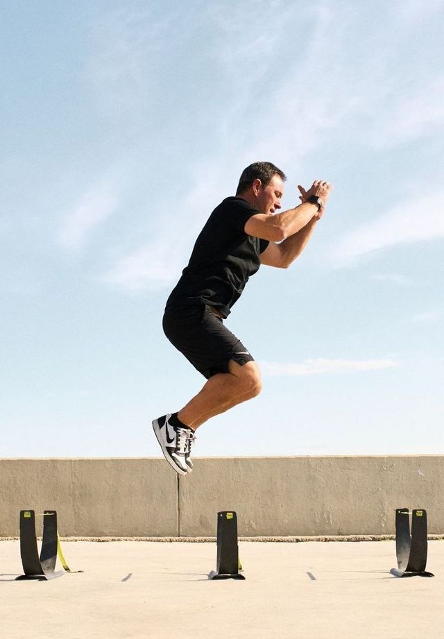 A man is jumping over hurdles on a sidewalk.