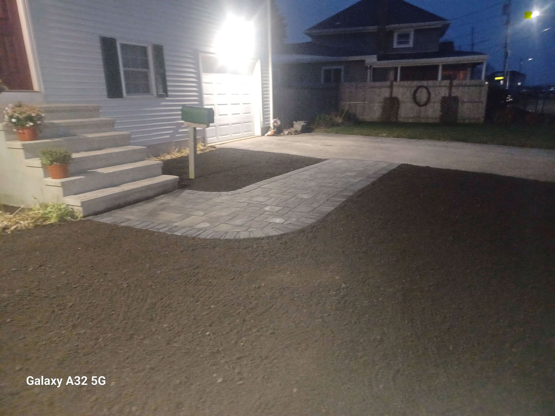 A white house with gray stairs and a stone walkway in front, illuminated by a bright porch light at dusk.