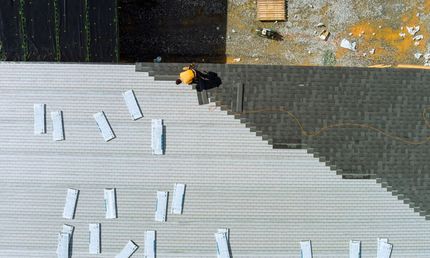 An aerial view of a man laying tiles on a roof.