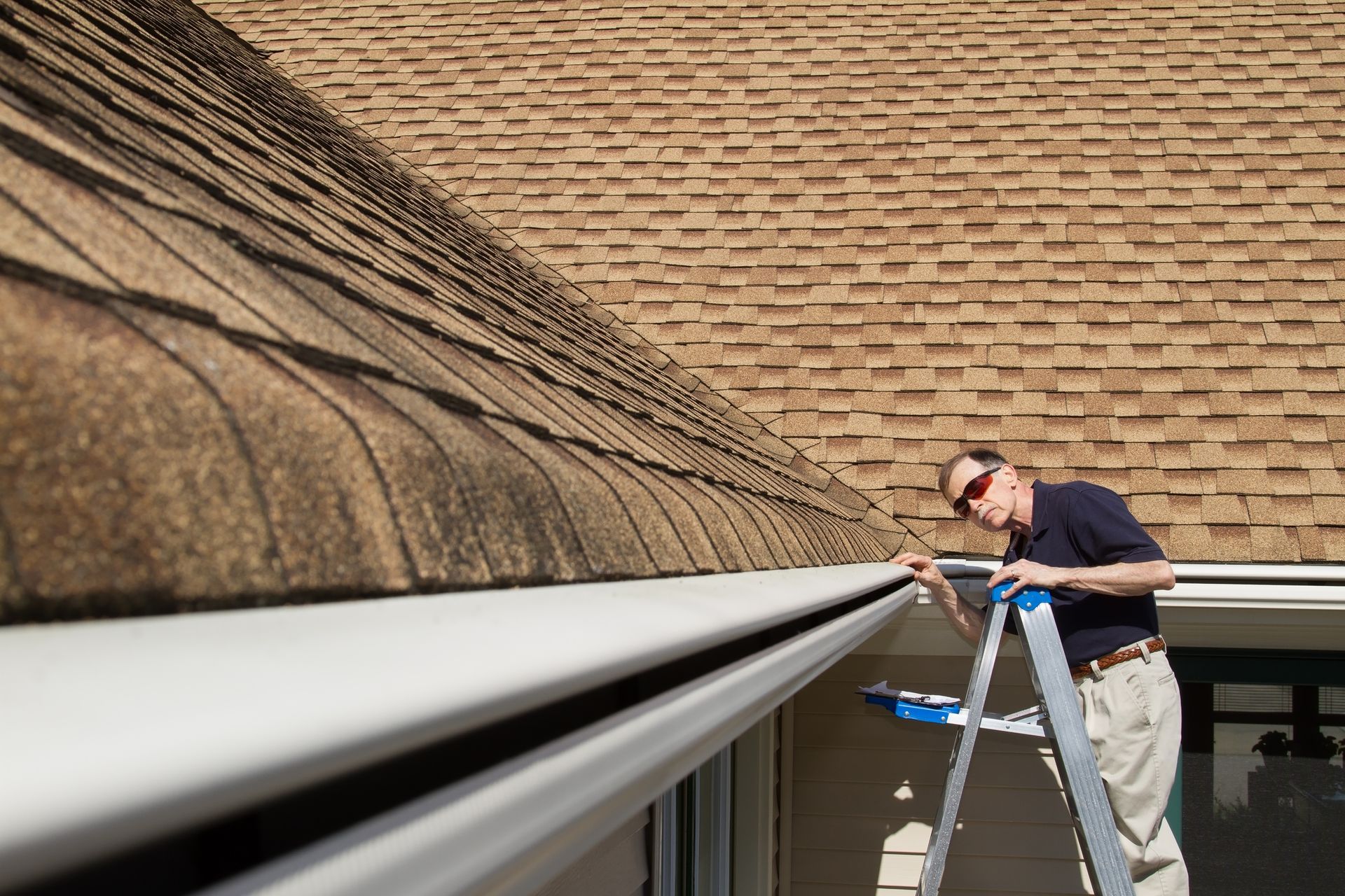 A man on a ladder is cleaning a gutter on the roof of a house.