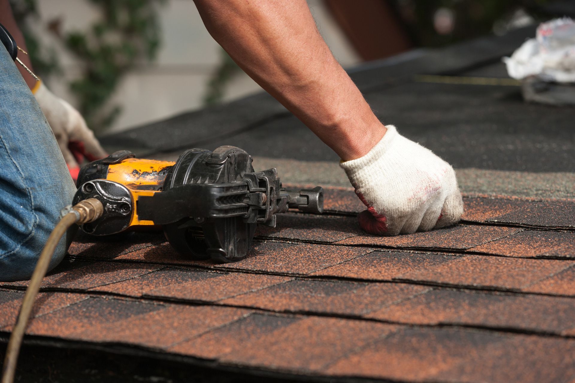 Close-up of a worker using a tool to fasten shingles on a roof.
