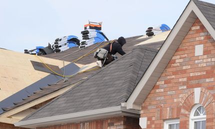 A man is working on the roof of a brick house.