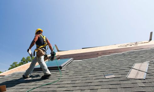 A man is standing on top of a roof holding a piece of wood.