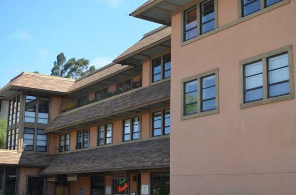 Multi-story building with peach-colored walls, brown roof, and multiple windows under a blue sky.