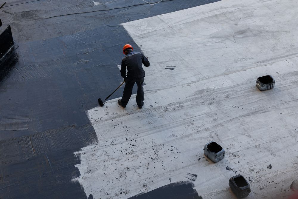 Person applying black sealant to a flat roof with a roller. White and black contrast.