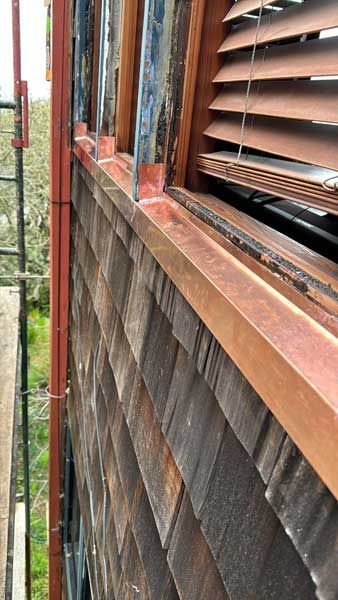 Copper guttering and flashing on a cedar shingle wall, next to a window with blinds.