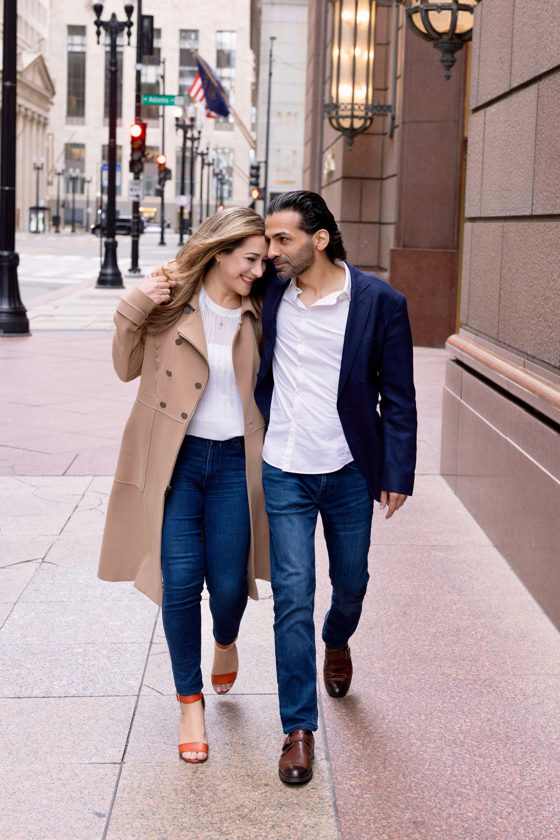 Couple walking arm in arm on a city sidewalk, wearing coats and jeans.