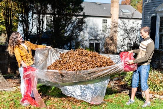 A man and a woman are standing next to a pile of leaves.