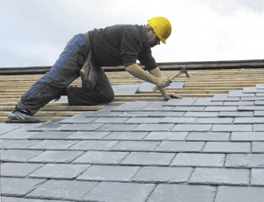 man in yellow hat with hammer working on a slate roof