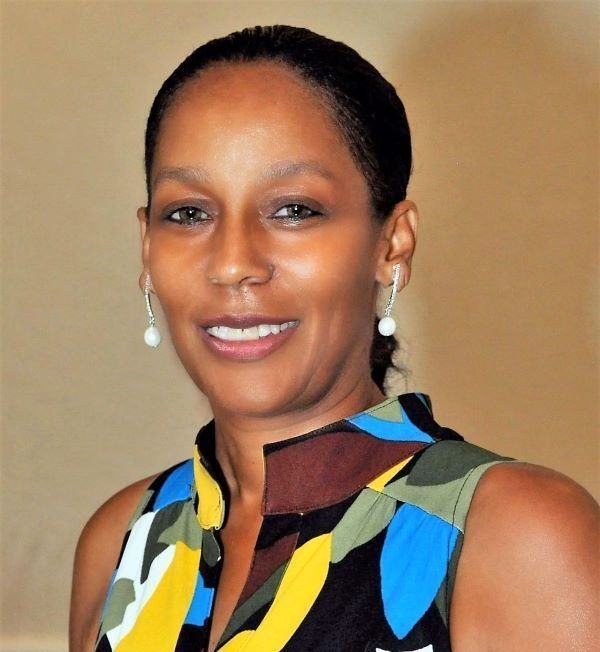 A woman wearing a colorful shirt and earrings smiles for the camera