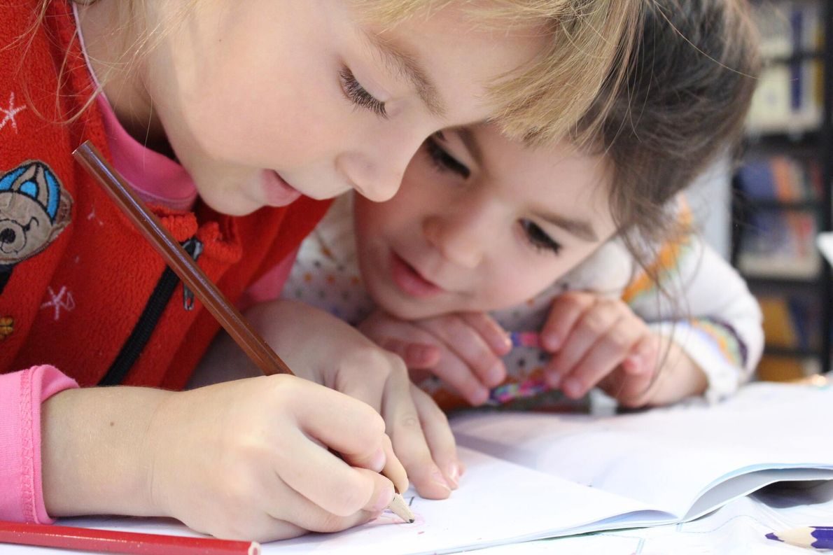 Two young girls are sitting at a table writing in a notebook.