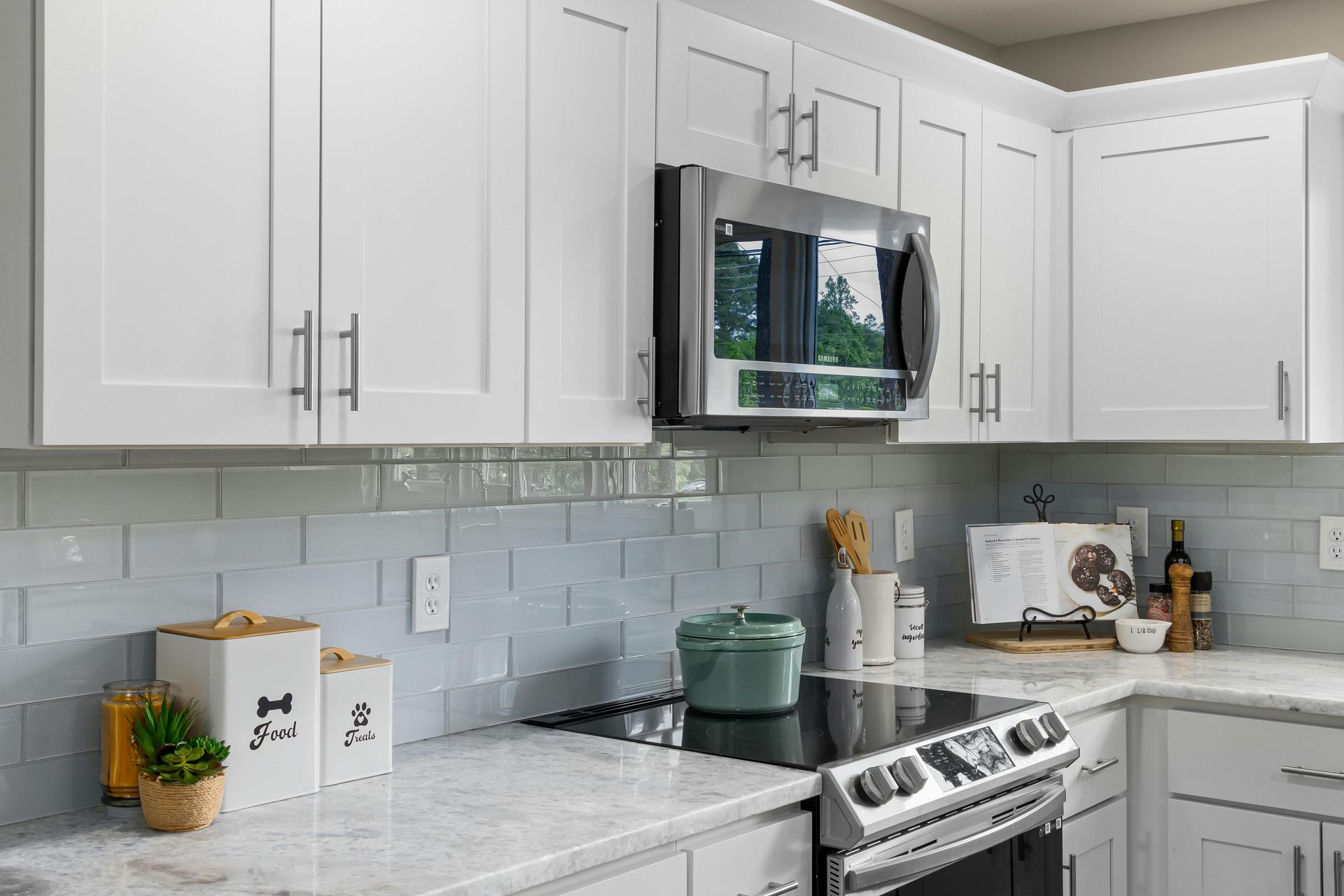 A kitchen with white cabinets , a stove , a microwave , and a pot on the counter.
