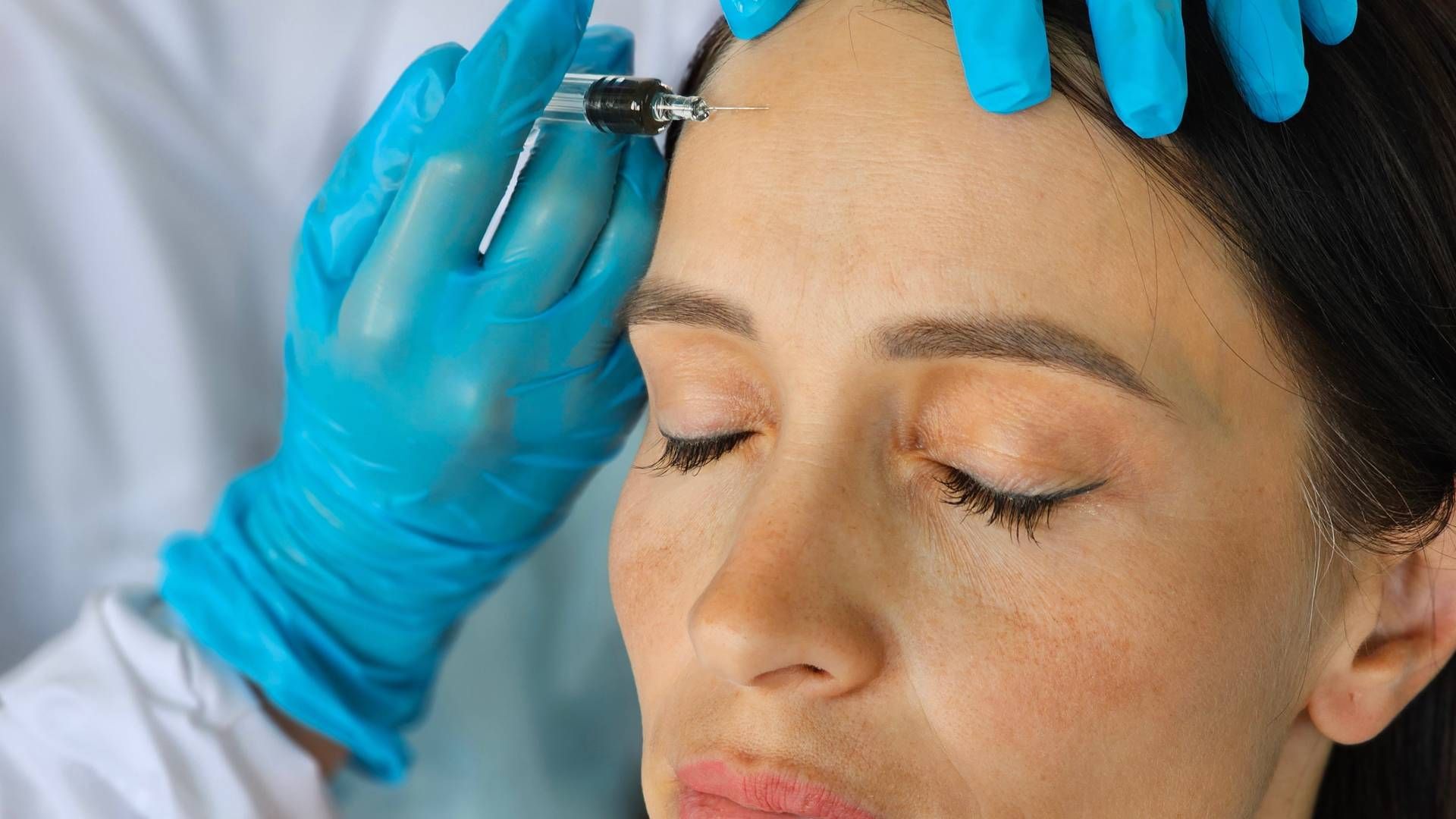 Person receiving an injection to forehead from gloved hands.