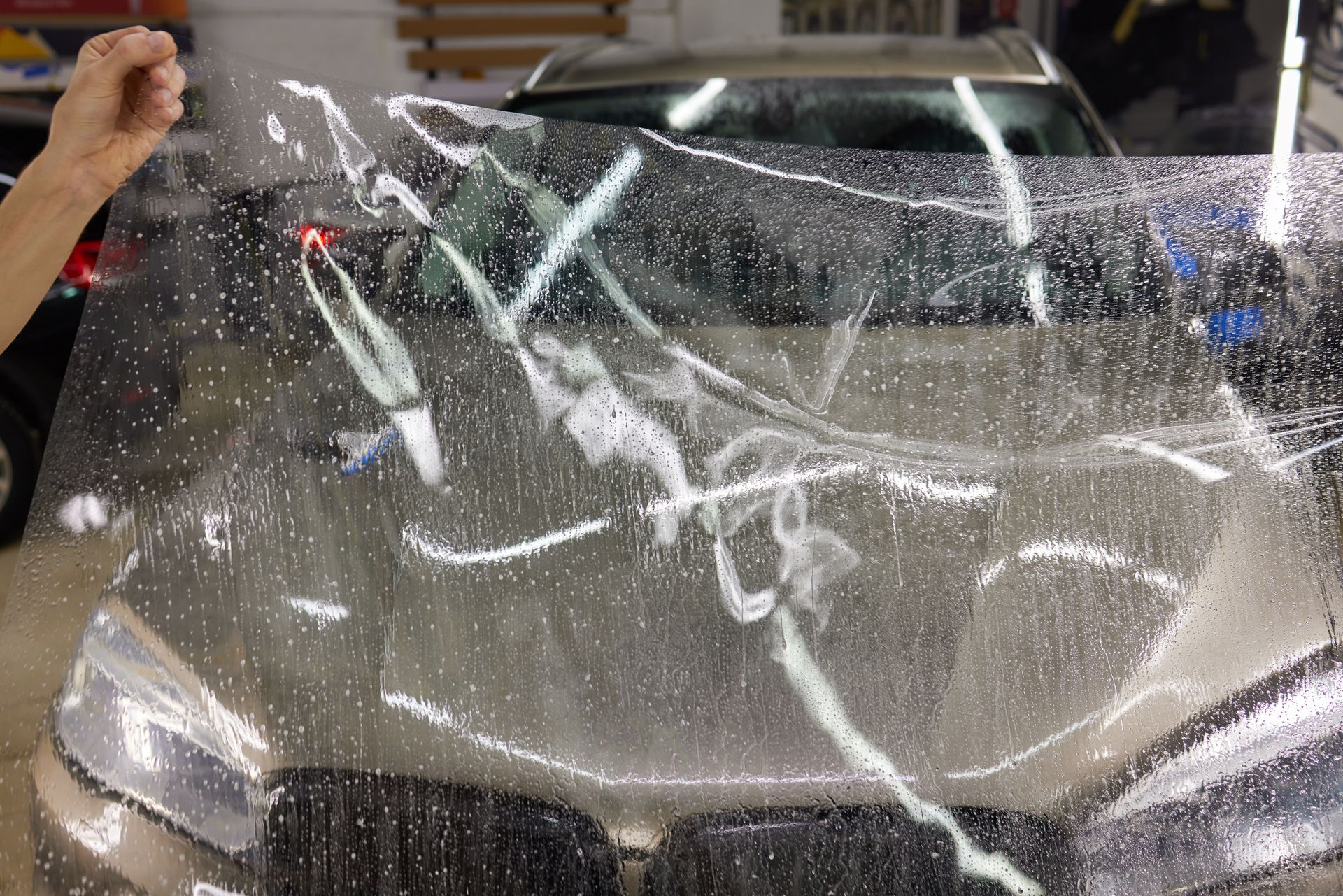 A person applying clear protective film to the hood of a car in a garage.