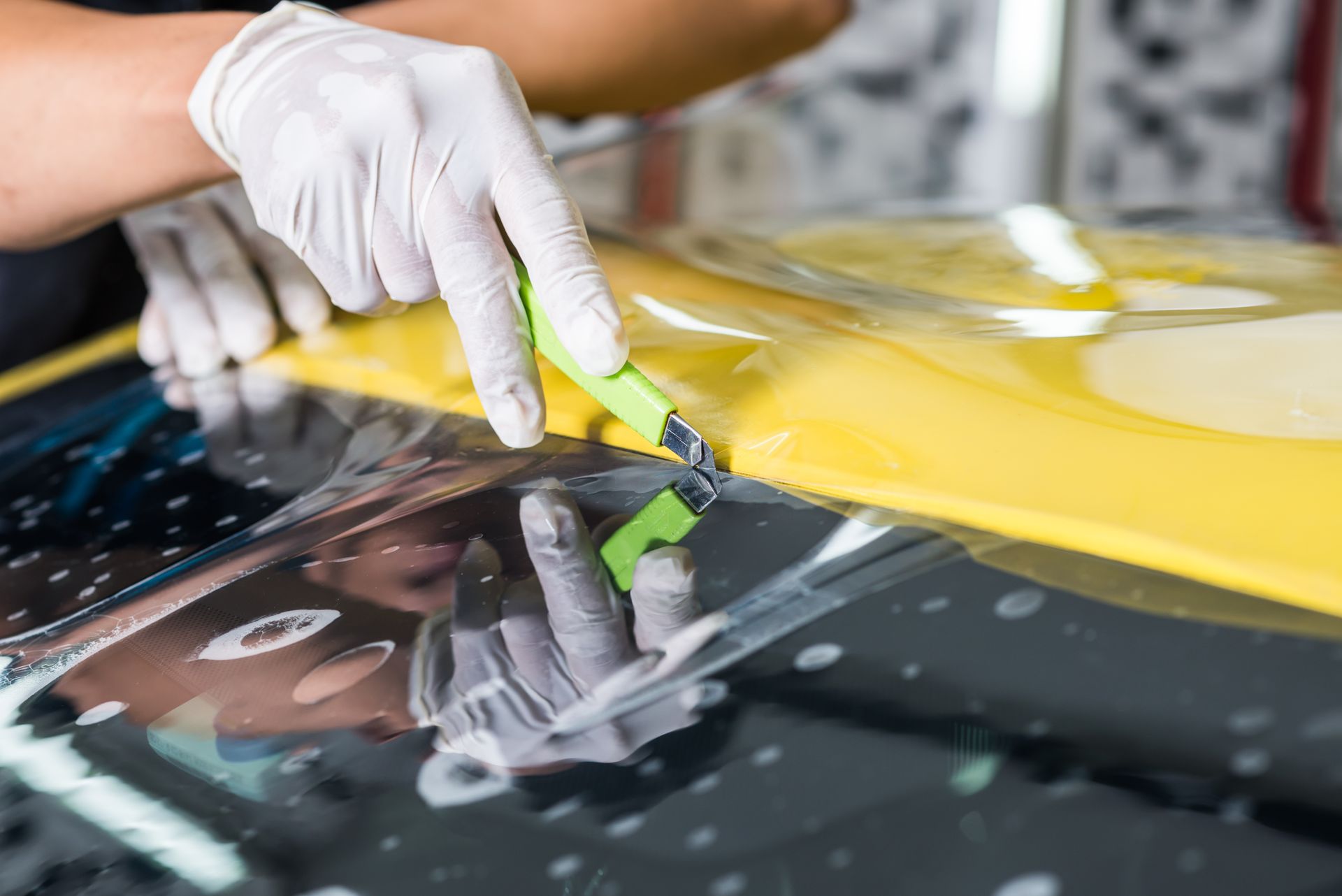 Person wearing gloves cutting yellow film on a car windshield.