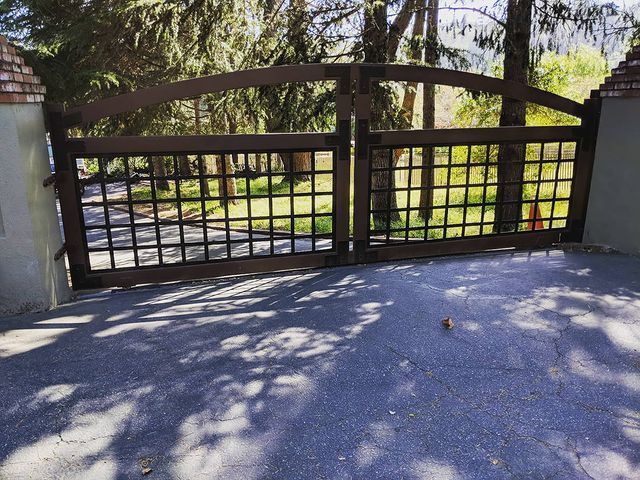 Wooden gated driveway with grid-like design, set against trees.