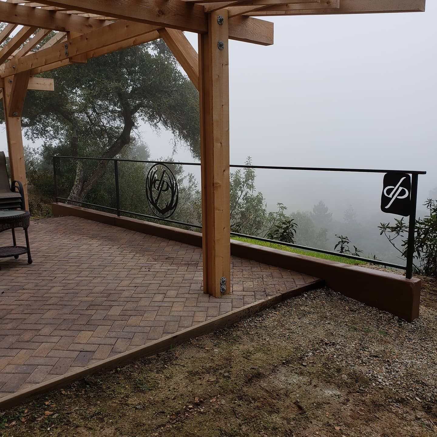 Wooden pergola and deck with metal railing, overlooking a foggy landscape.