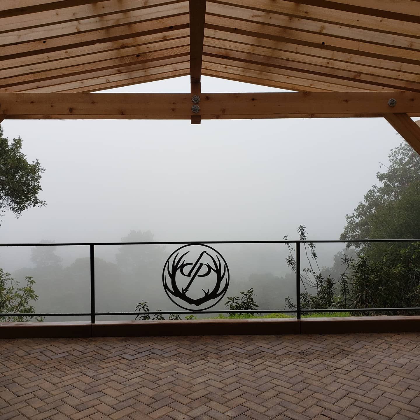 A covered wooden patio with a logo on the railing overlooks a foggy landscape.