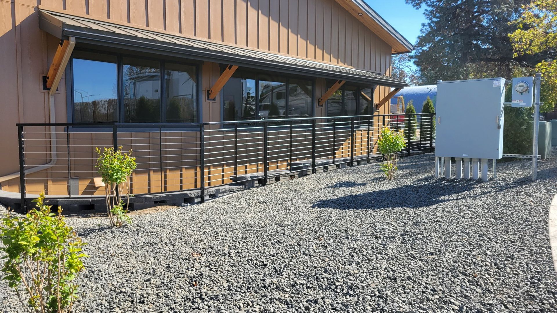 Building exterior with windows, deck railing, gravel, and small bushes.
