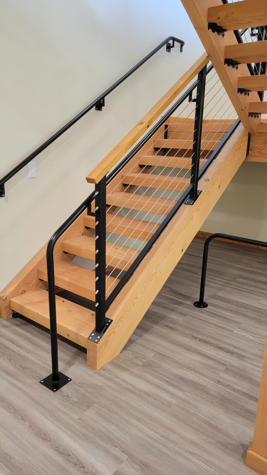 Wooden staircase with black metal handrails and cable infill, indoors.