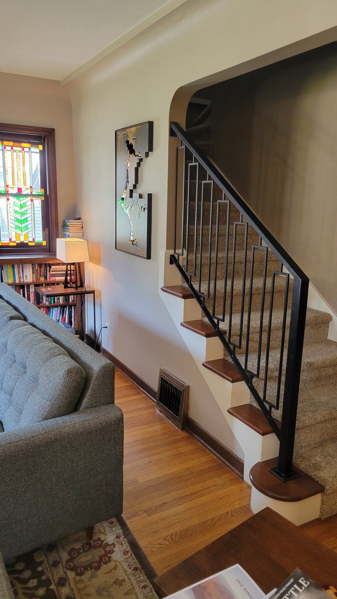 Interior view of a living room with stairs.  A wooden floor leads to a carpeted staircase with a black handrail.