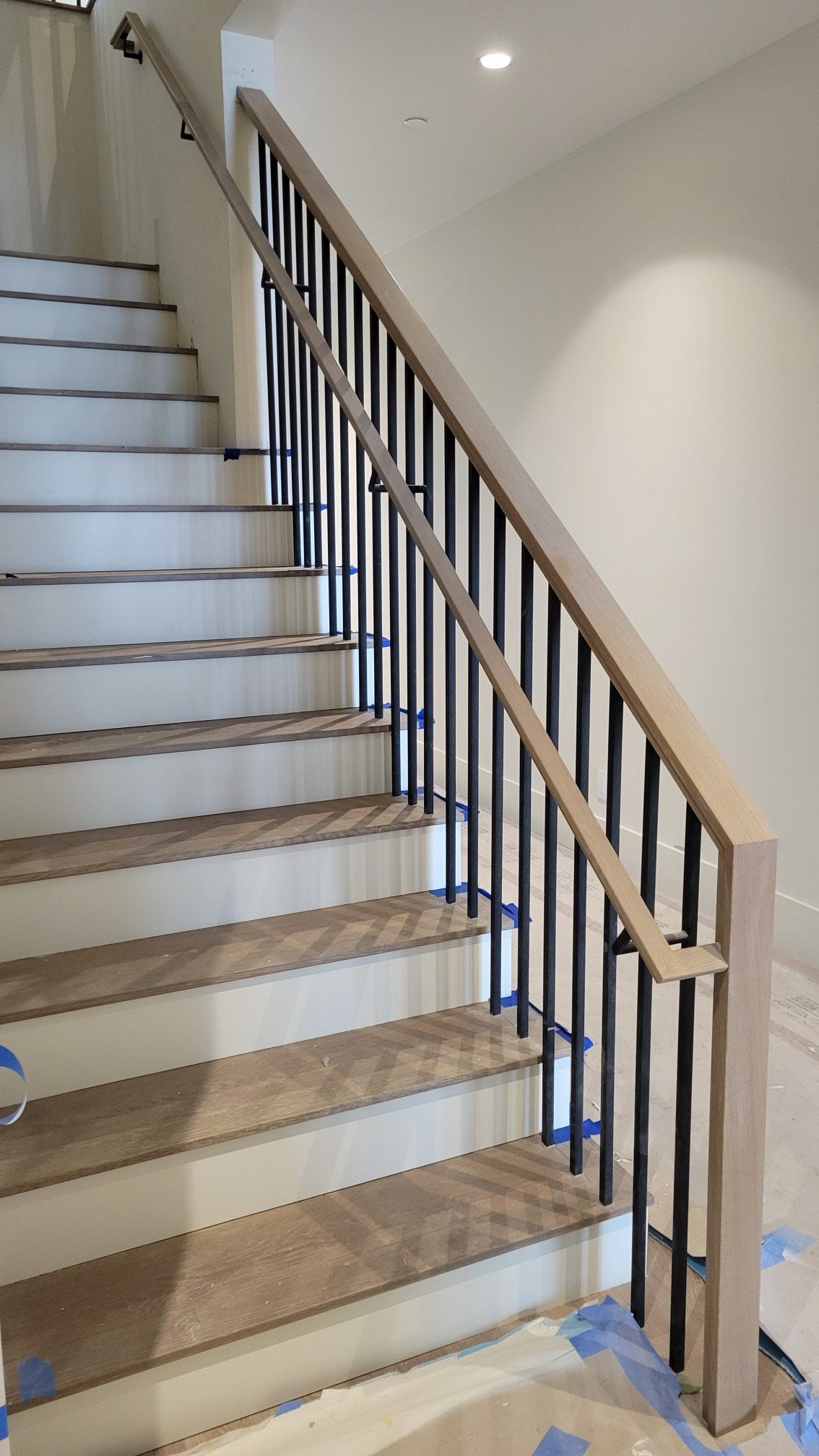 Staircase with wooden steps and railing, black spindles, and light-colored walls.