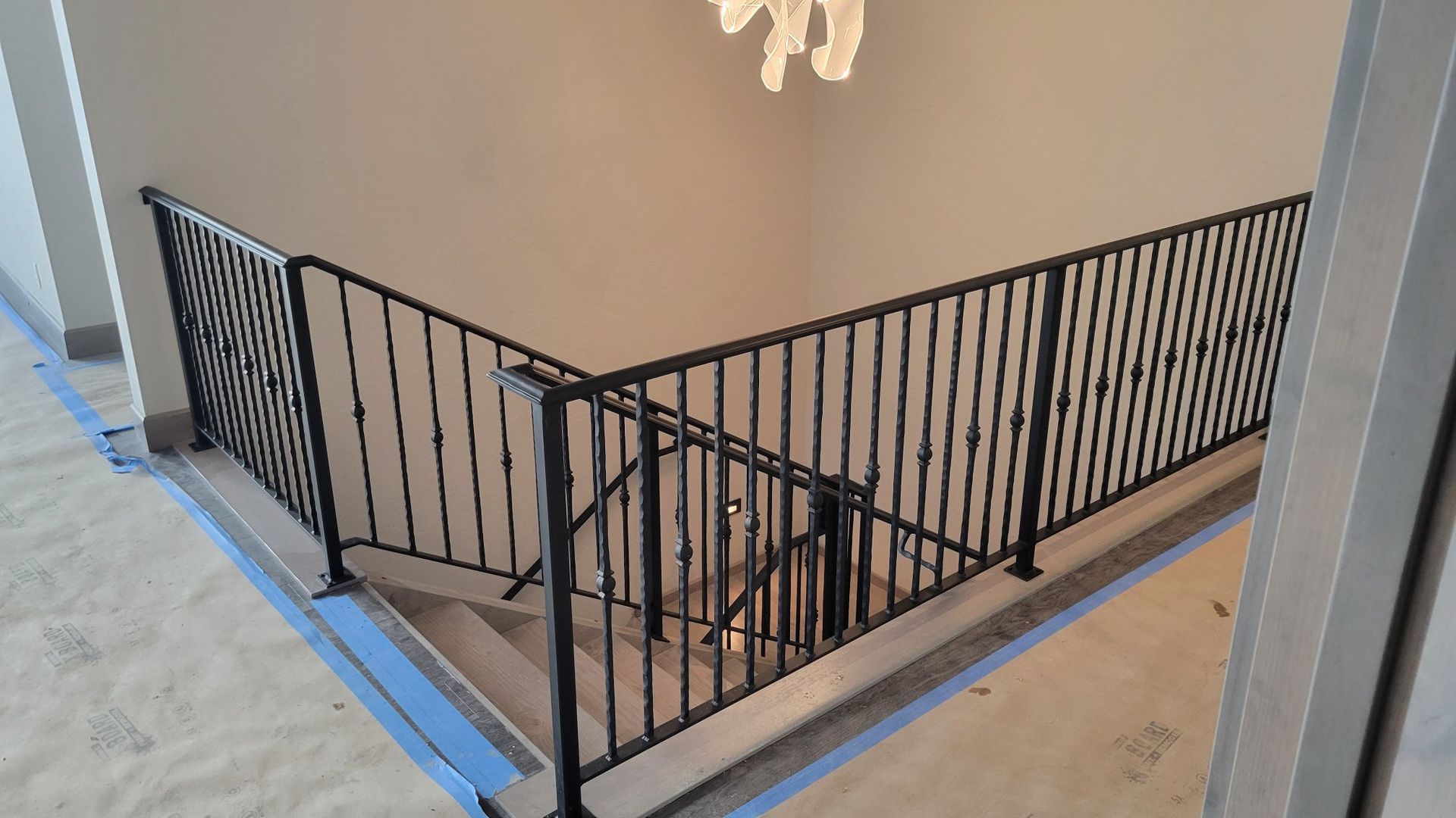 Black metal railing along a staircase, viewed from above, in a beige-walled interior.