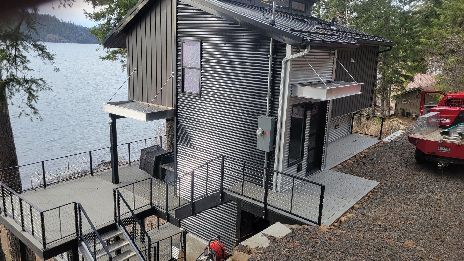 Modern metal-clad house by water with deck, stairs, and truck.