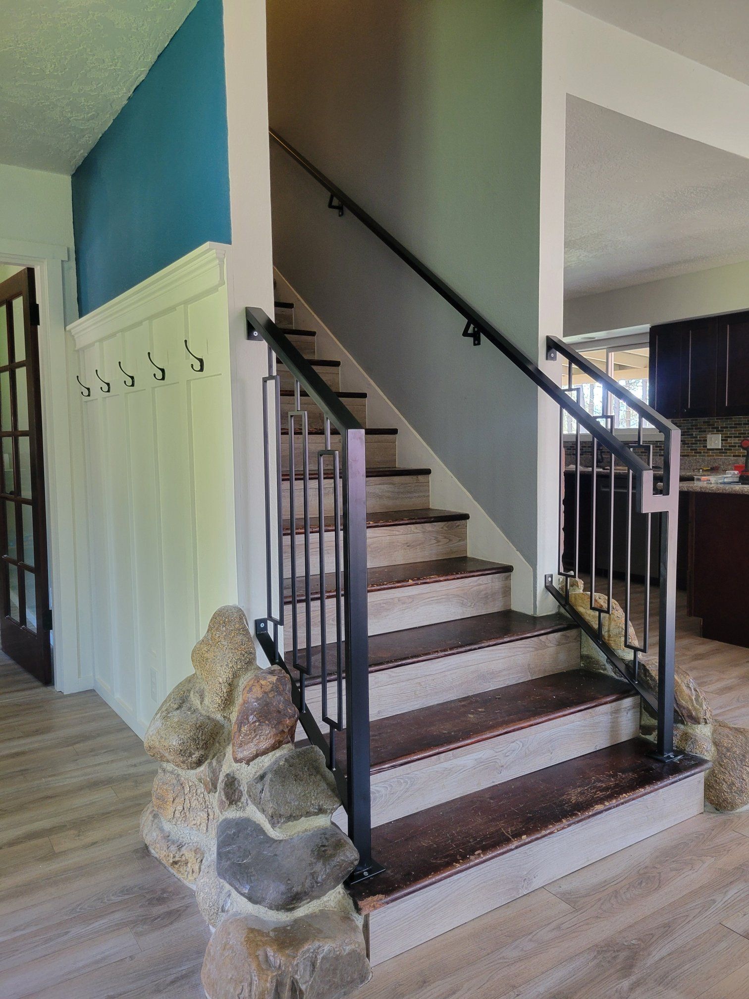 Staircase with black metal railing, wooden steps, and stone base in a home setting.