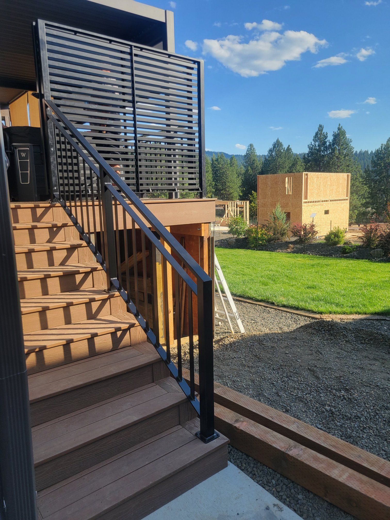 Wooden outdoor staircase with black railing leads up to a deck with privacy screen; construction in background.