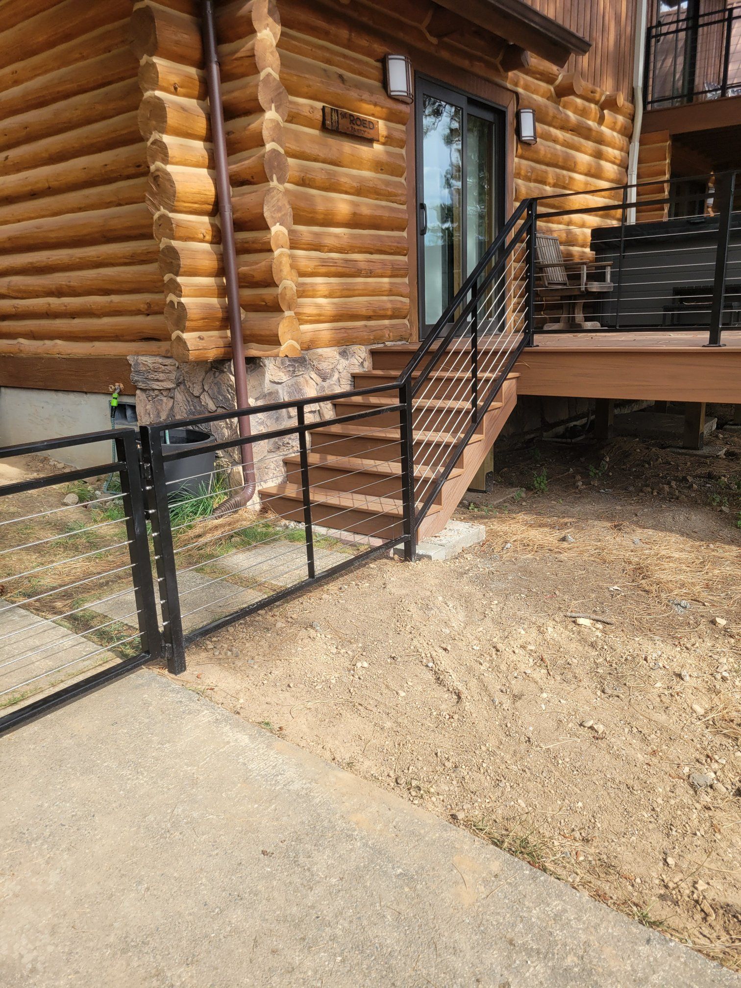 Wooden steps and black metal railings leading to a cabin entrance. Gravel and concrete path in the foreground.