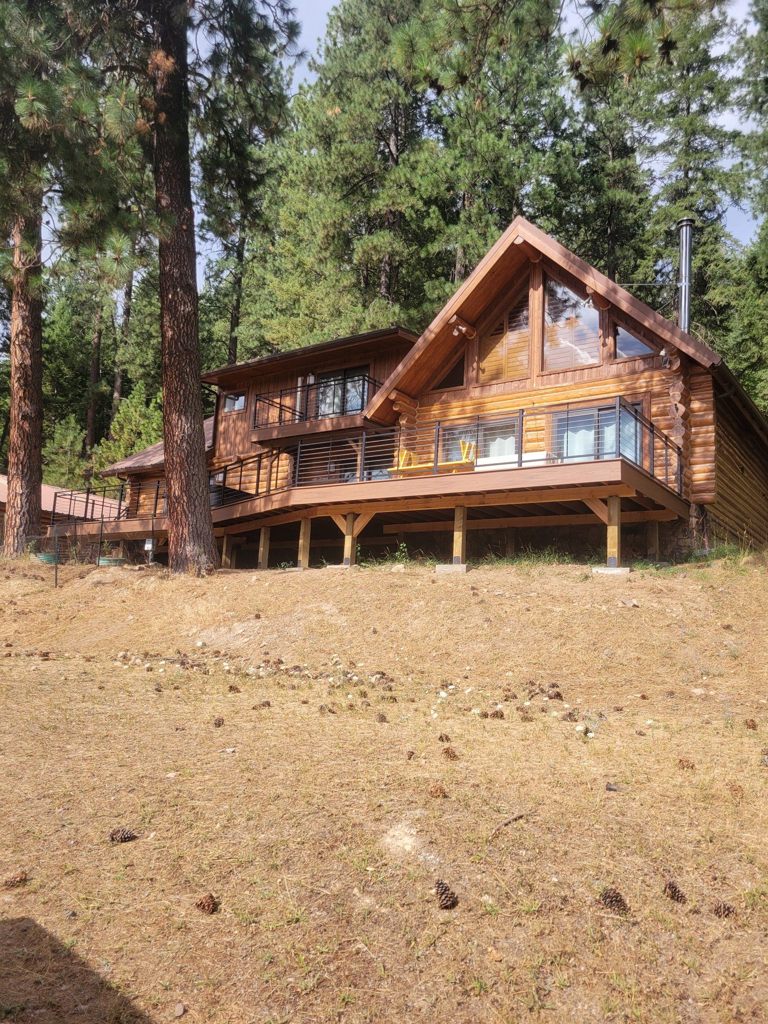 Log cabin house with a large deck and tall windows surrounded by trees.