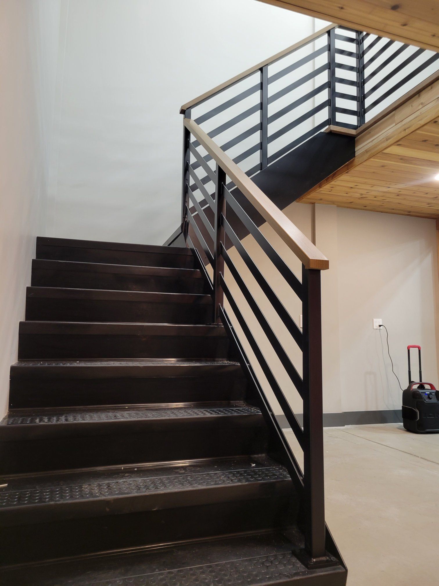 Staircase with black metal railings and treads, wooden handrails, leading upwards.