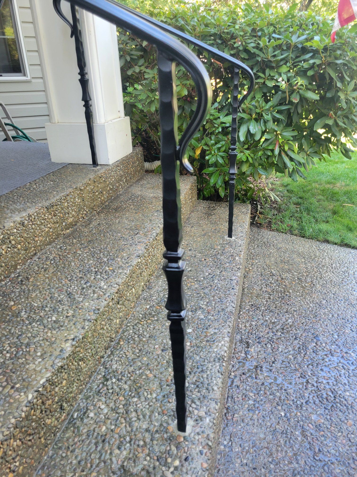 Black wrought iron handrail on concrete steps leading to a house entrance.